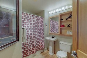 Un baño con cortina de ducha estampada, lavamanos, inodoro y tocador con espejo e iluminación.