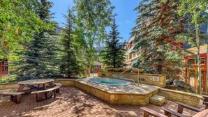 An outdoor patio with a hot tub, picnic tables, and wooden benches. - 1 Bedroom Mountain Condo in River Run Village with Beautiful Mountain Views and Walking Distance to Ski (Keystone)