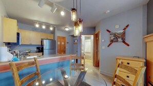 A modern kitchen with wooden cabinets, a glass dining table, and pendant lighting. - 1 Bedroom Mountain Condo in River Run Village with Beautiful Mountain Views and Walking Distance to Ski (Keystone)