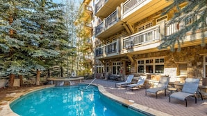 A pool area with lounge chairs and a stone building with balconies. - Premier 2 Bedroom Ski in, Ski out Lone Eagle Condo With the Best Access to Skiing in Keystone (Keystone)
