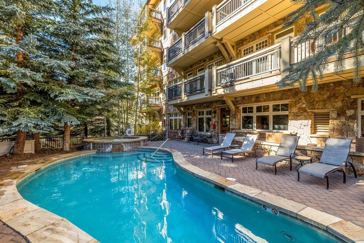 Un área de piscina con sillones reclinables y un edificio de piedra con balcones.