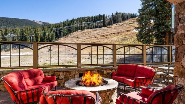 A patio with red chairs and a stone fire pit, overlooking a forested hillside. - Premier 2 Bedroom Ski in, Ski out Lone Eagle Condo With the Best Access to Skiing in Keystone (Keystone)