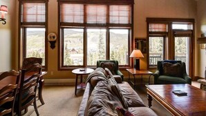 A cozy living room with a sofa, chairs, a coffee table, and large windows offering a view of the outdoors. - Premier 4 Bedroom Ski in, Ski out Lone Eagle Condo With the Best Access to Skiing in Keystone (Keystone)
