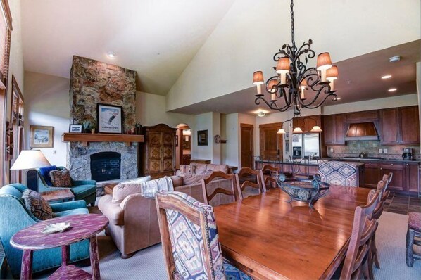 A spacious living room with a fireplace, a dining area with a large wooden table, and a kitchen with wooden cabinets. - Premier 4 Bedroom Ski in, Ski out Lone Eagle Condo With the Best Access to Skiing in Keystone (Keystone)