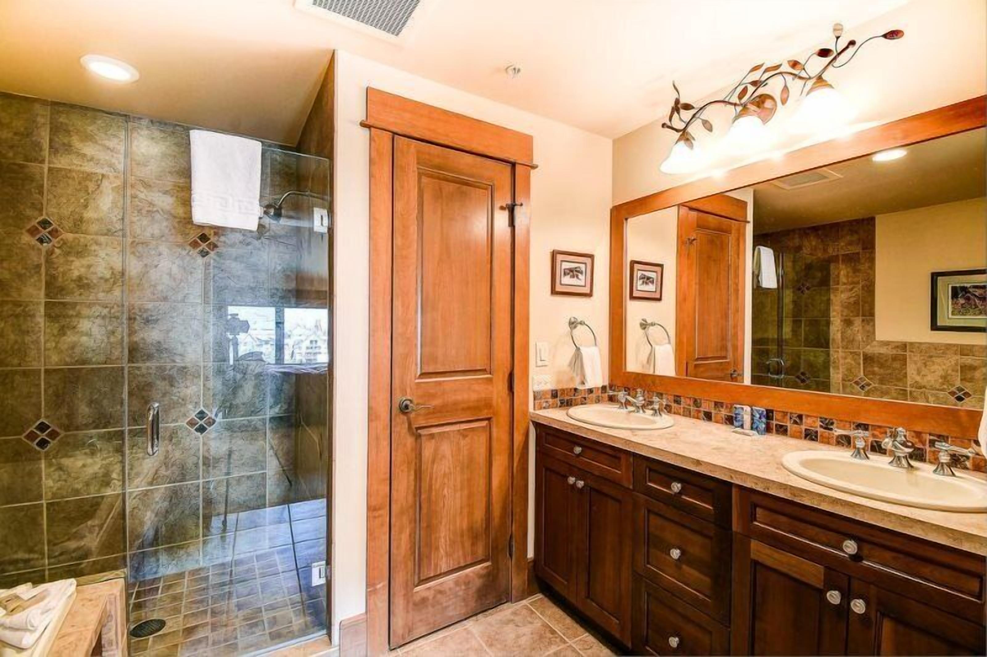 A bathroom with a glass-enclosed shower, wooden vanity with two sinks, and a large mirror.
