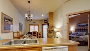 A compact kitchen with a dishwasher, wooden cabinets, and a dining area with chairs and a table. - 1 Bedroom Colorado Vacation Rental in River Run Village Steps from the Summit Express Gondola (Keystone)