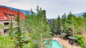 A pool area with lounge chairs and umbrellas, surrounded by trees and a mountain view. - 1 Bedroom Colorado Vacation Rental in River Run Village Steps from the Summit Express Gondola (Keystone)