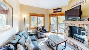A cozy living room with a stone fireplace, a large TV, and a comfortable seating area with a sofa and a table. - 1 Bedroom Colorado Vacation Rental in River Run Village Steps from the Summit Express Gondola (Keystone)