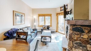 A living room with a stone fireplace, a sofa set, a coffee table, and a dining table. - 1 Bedroom Colorado Vacation Rental in River Run Village Steps from the Summit Express Gondola (Keystone)