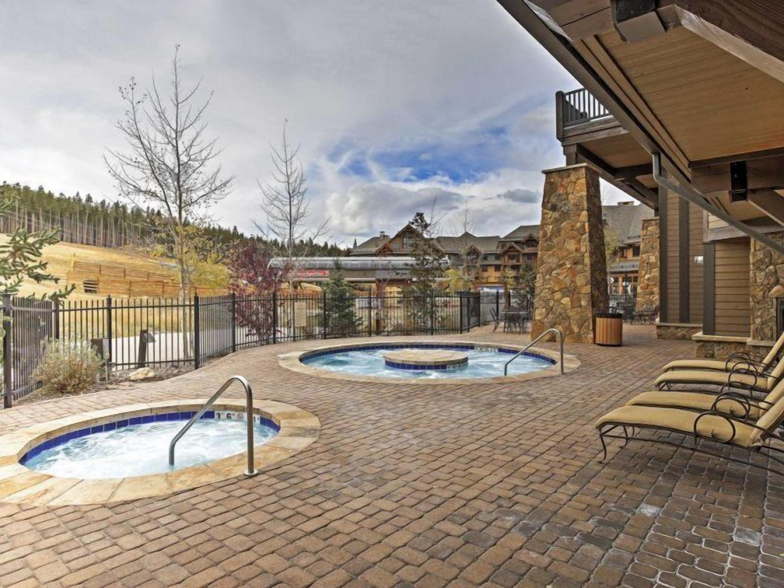 A pool area with two hot tubs, a stone wall, and lounge chairs.