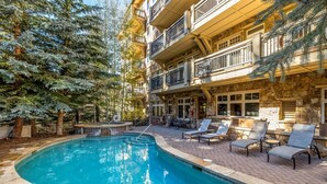 A pool area with lounge chairs and a stone building with balconies. - Premier 3 Bedroom Ski in, Ski out Lone Eagle Condo With the Best Access to Skiing in Keystone (Keystone)