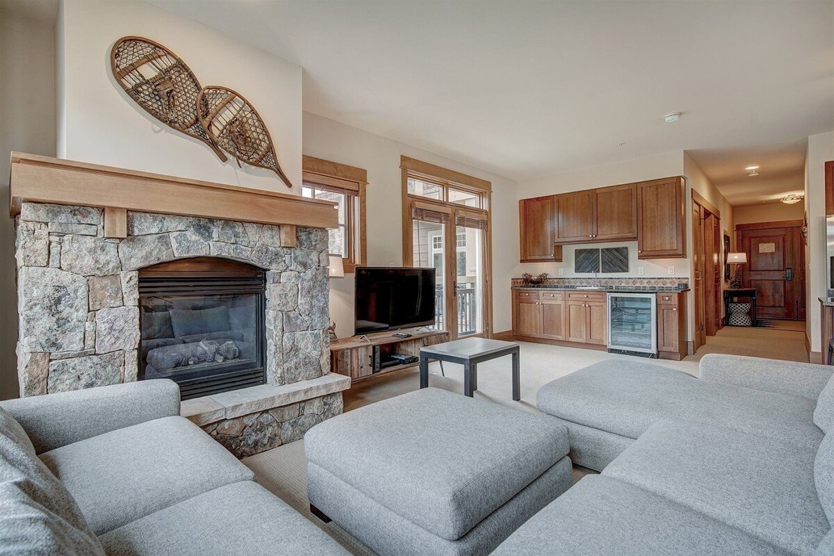 A living room with a stone fireplace, grey sofas, and a television.