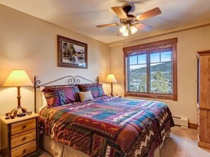 Une chambre à coucher comprenant un lit, deux lampes de chevet, un ventilateur de plafond, une fenêtre avec vue et une armoire en bois.