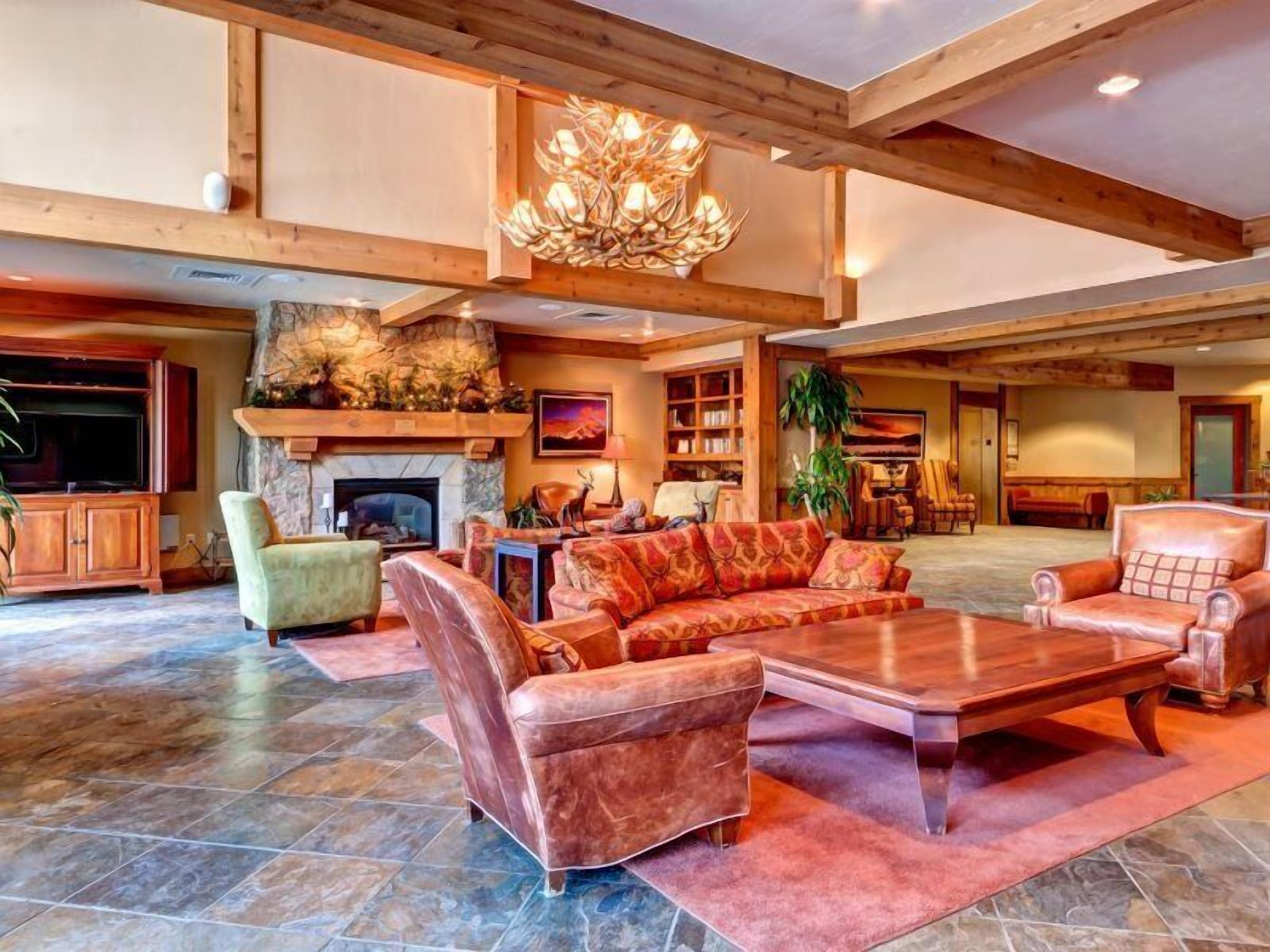 A spacious living area with a fireplace, leather sofas, a large wooden coffee table, and a chandelier.