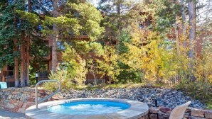 A hot tub surrounded by stone walls and a chair, set in a garden with trees and a building in the background. - Luxury 3 Bedroom Mountain Vacation Rental in Breckenridge Just Two Blocks From Downtown (Breckenridge)