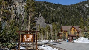 A wooden sign reading "SKI TIP RANCH" in front of a lodge with a mountain backdrop. - Family Friendly 3 Bedroom Mountain Vacation Rental in Keystone With Complimentary Shuttle Service and Hot Tub Access (Keystone)