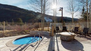 Zona de piscina con un jacuzzi, mobiliario exterior y vistas a una montaña boscosa.