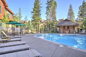 A pool area with lounge chairs, a small building, and tall pine trees. - Luxury 2 Bedroom Mountain Vacation Rental in Breckenridge With Access to a Hot Tub and Heated Garage Parking (Breckenridge)