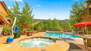 A hot tub with a pool, outdoor seating, and a view of a forested area. - 1 Bedroom Premier Mountain Condo in River Run Village Just a Short Walk to Shopping, Dining, and Skiing (Keystone)