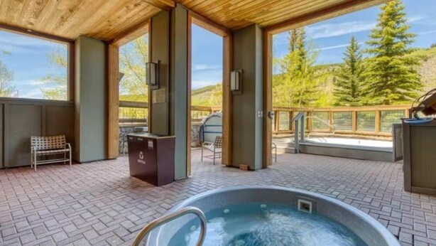 A wooden deck with a hot tub, seating area, and a view of trees. - 1 Bedroom Premier Mountain Condo in River Run Village Just a Short Walk to Shopping, Dining, and Skiing (Keystone)