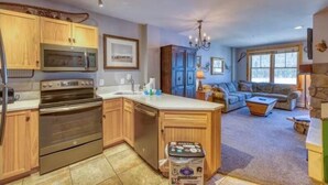 A kitchen with wooden cabinets, a built-in microwave, and a stainless steel oven. There is a dining area with a table and chairs, and a living room with a sofa and a coffee table. - 1 Bedroom Premier Mountain Condo in River Run Village Just a Short Walk to Shopping, Dining, and Skiing (Keystone)