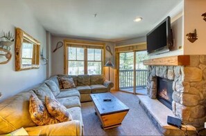 A cozy living room with a stone fireplace, a large window, and a television mounted above it. - 1 Bedroom Premier Mountain Condo in River Run Village Just a Short Walk to Shopping, Dining, and Skiing (Keystone)