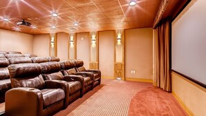 A theater room with rows of leather recliner seats, a carpeted floor, and a large screen wall.