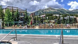 A pool area with lounge chairs and a hot tub, surrounded by buildings and mountains.