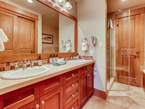 Un baño con dos lavamanos, armarios de madera, un espejo grande y zona de ducha.