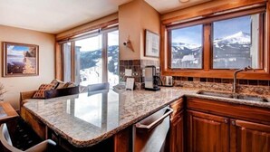 A kitchen with a granite countertop, wooden cabinets, and large windows offering a mountain view. - 1 Bedroom Ski in, Ski out Mountain Vacation Rental Located Next to Historic Main Street in Downtown Breckenridge (Breckenridge)