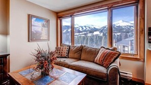 A cozy living room with a large window offering a mountain view, a wooden coffee table, and a comfortable sofa. - 1 Bedroom Ski in, Ski out Mountain Vacation Rental Located Next to Historic Main Street in Downtown Breckenridge (Breckenridge)