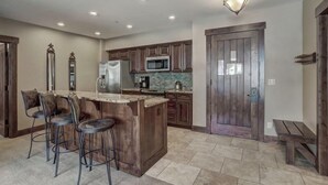 A kitchen with a central island, bar stools, wooden cabinets, a microwave, and a door with a rustic design.