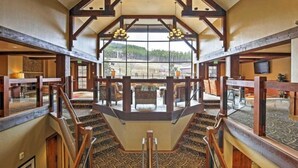 A hotel interior with a central staircase, wooden beams, and a large window offering a view of the outdoors.