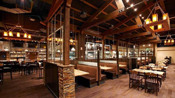 Un restaurant doté de poutres en bois, de piliers en pierre et de plusieurs espaces de restauration, notamment des banquettes et des tables.