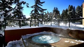 A hot tub surrounded by snow-covered trees and a clear blue sky.