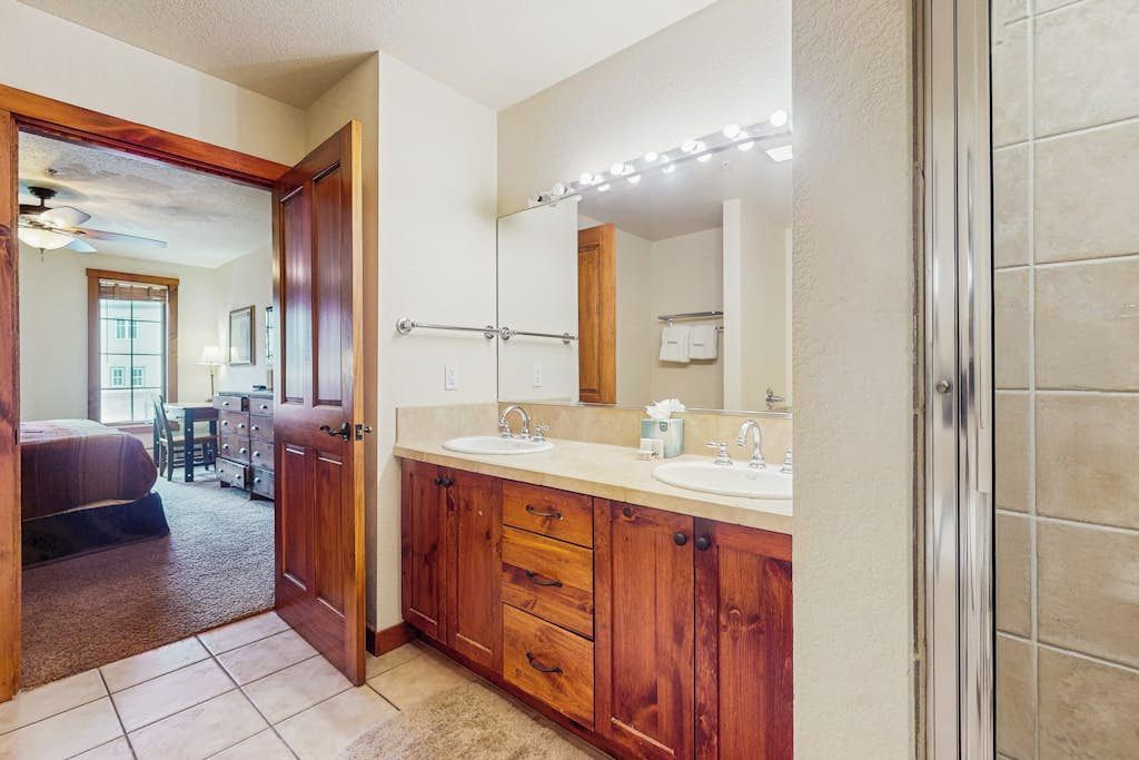 A bathroom with wooden cabinets, a double sink, and a mirror with lights.