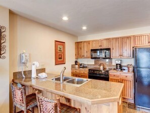 A kitchen with wooden cabinets, a granite countertop, a stainless steel sink, a microwave, a stove, and a refrigerator. - Luxury 1 Bedroom Mountain Vacation Rental in Breckenridge With Access to a Hot Tub and Heated Garage Parking (Breckenridge)