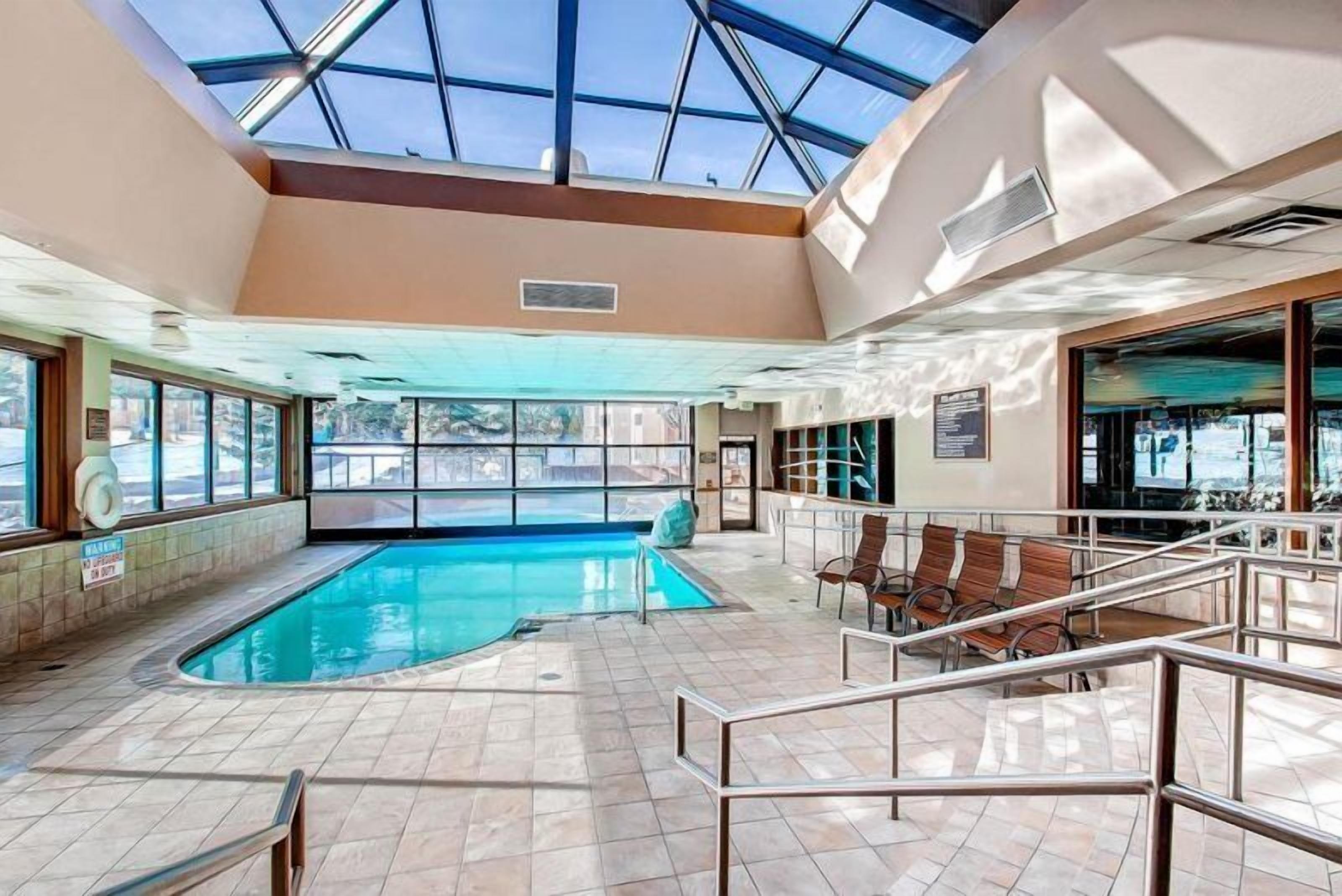 An indoor swimming pool with a glass ceiling, seating areas, and a view of the outside.