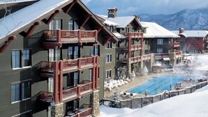 Un hotel de varios pisos con balcones, una zona de piscina y montañas al fondo.