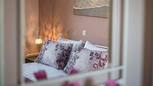 Quarto com cama, almofadas, mesa de cabeceira, luminária e pintura de um pôr do sol sobre o oceano.