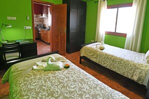 A room with two beds, a desk, a chair, a microwave, and a kitchenette.