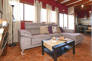 A living room with a sofa, a coffee table with pastries, a floor lamp, and a kitchen in the background.