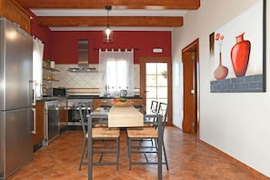 A kitchen with a dining area, wooden ceiling beams, a tiled floor, and a painting on the wall.