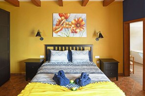 A bedroom with a bed, two bedside tables, a painting of flowers, and a yellow blanket. - Villa Mica inTijarafe (Tijarafe)