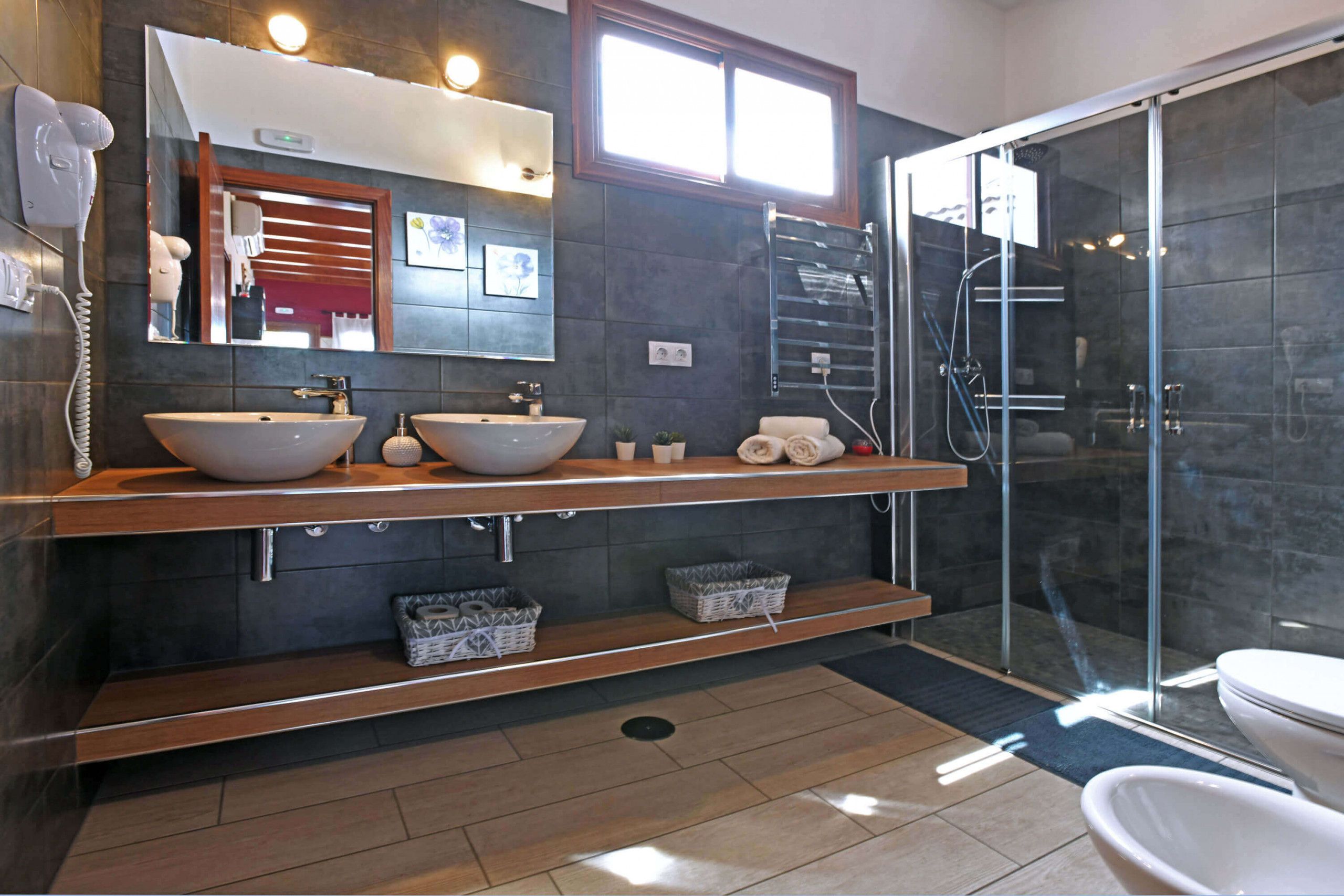 A modern bathroom with two sinks, a large mirror, a hairdryer, and a glass shower enclosure.