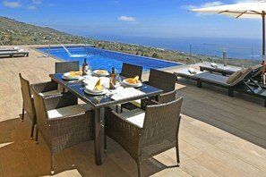 A dining table with chairs, a pool, and a view of the sea. - Villa Mica inTijarafe (Tijarafe)