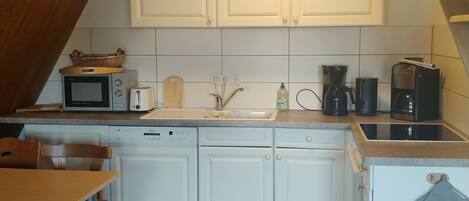 A compact kitchen with white cabinets, a Bosch dishwasher, a microwave, a toaster, a coffee maker, and a sink.