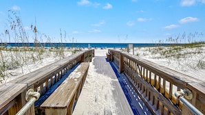 Une promenade en bois menant à une plage de sable où la végétation est clairsemée.