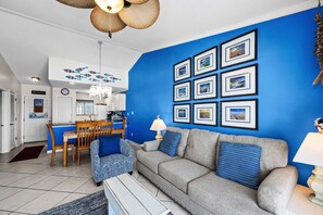 Una sala de estar con una pared de acento azul, un sofá gris y un comedor con una mesa y sillas de madera.