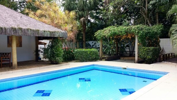 A swimming pool with a thatched roof structure nearby, surrounded by lush greenery. - 4 suites WITH AIR CONDITIONING + 1 bedroom-living room with bathroom 2 refrigerators barbecue garden terrace TV DVD YT (São Sebastião)